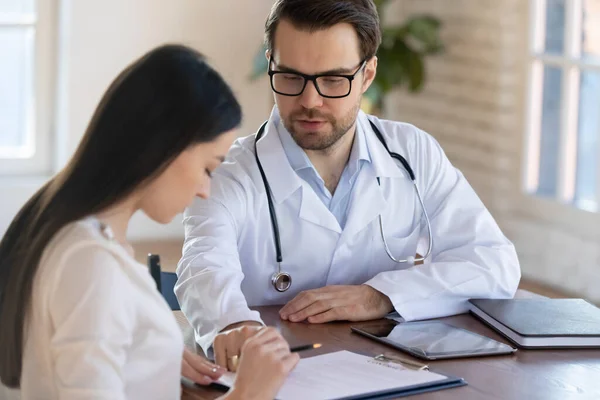Kvinnelig pasient signerer papirkontrakt på møte med legen – stockfoto