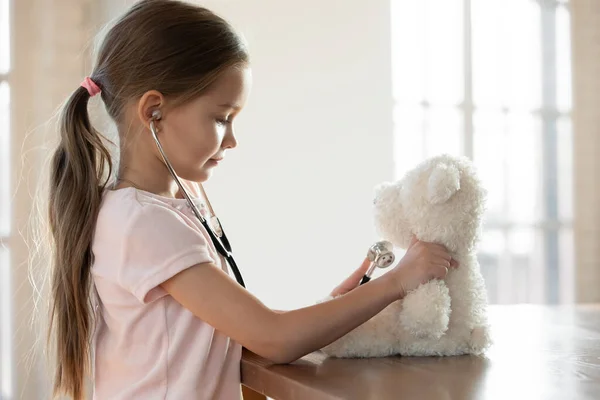 Pieni tyttö pelata lääkäri peli pehmo lelu kotona — kuvapankkivalokuva