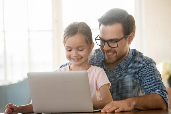 Smiling dad and little daughter watch video on laptop