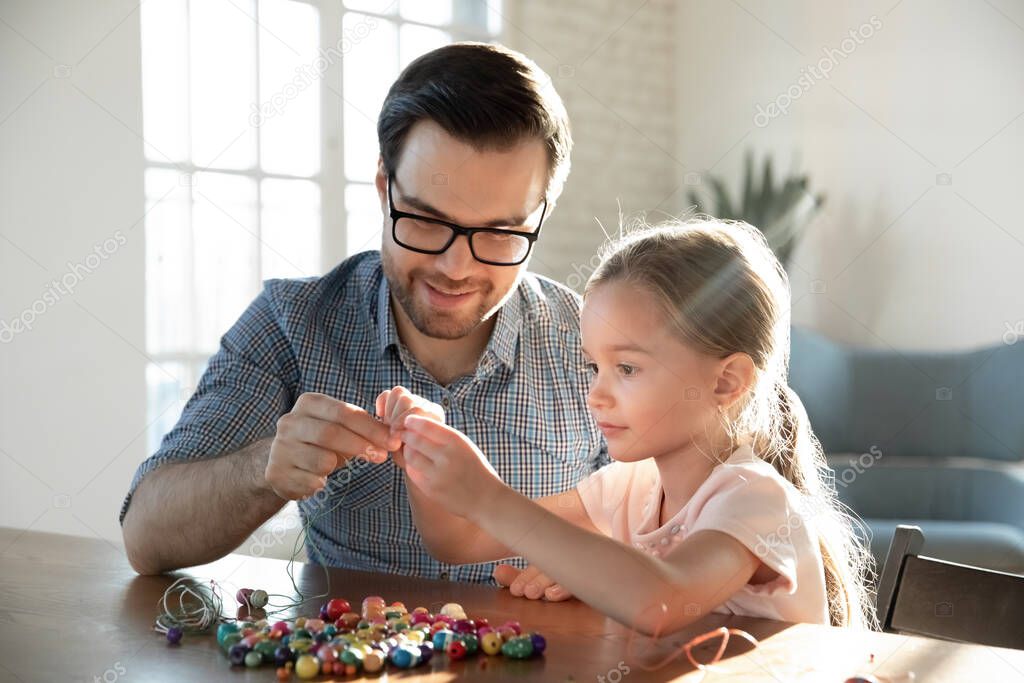 Loving dad and small daughter make wooden bracelets together