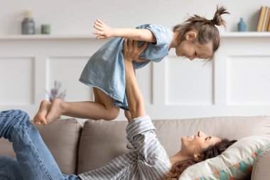 Gülen bir anne kucağında küçük bir kız, kanepede komik oyunlar oynuyor.