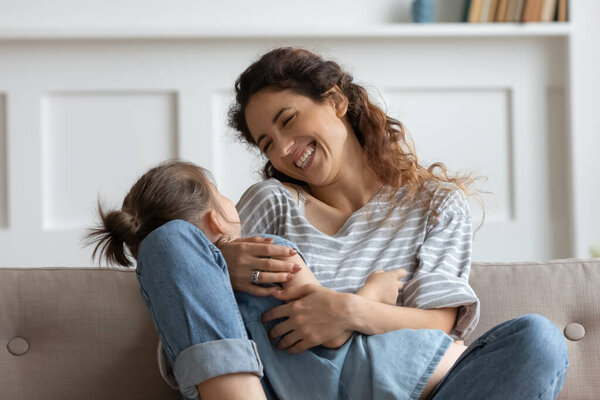Smiling young mother holding little daughter, sitting on couch