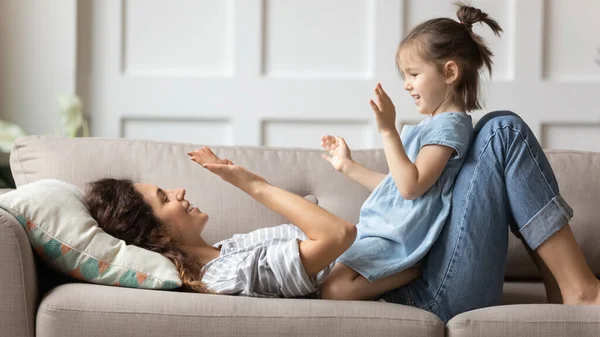 Smiling mother playing with little daughter, clapping hands on couch — Stock Photo, Image