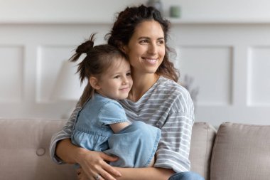 Gülümseyen anne küçük kızı kucaklıyor, bir kenara bakıyor, hayal kuruyor.
