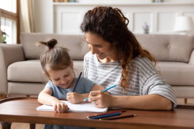 Gülümseyen anne ve küçük kız oyun oynuyor, renkli kalemler çiziyorlar.