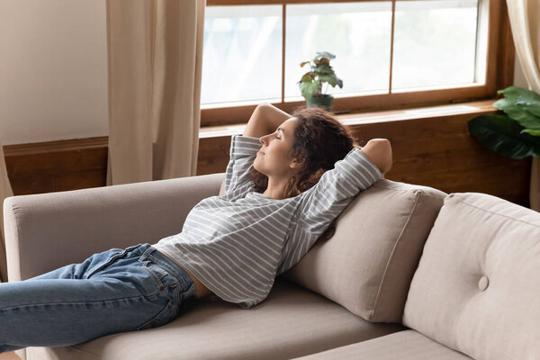 Peaceful calm young woman relaxing on cozy couch alone