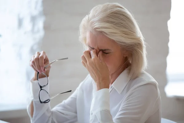 Mujer de mediana edad cansada sufre de dolor de cabeza en la oficina —  Fotos de Stock