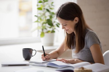 Gülümseyen milenyum kızı evde ders çalışıp notlar alıyor.