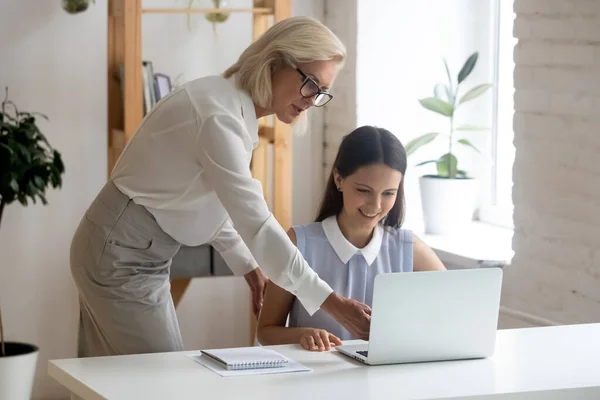 Confident middle-aged businesswoman help intern working on laptop — Stock Photo, Image
