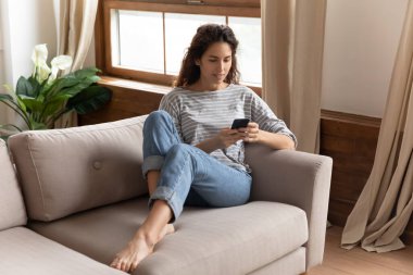 Güzel, genç bir kadın telefon kullanıyor ve kanepede dinleniyor.