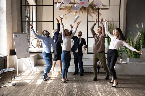 Excited diverse business people throwing papers, celebrating teamwork success