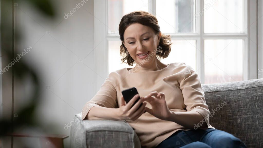 Smiling mature woman texting on smartphone at home