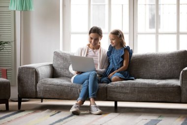 Mutlu anne ve küçük kız kanepede dizüstü bilgisayar kullanarak rahatlayın.