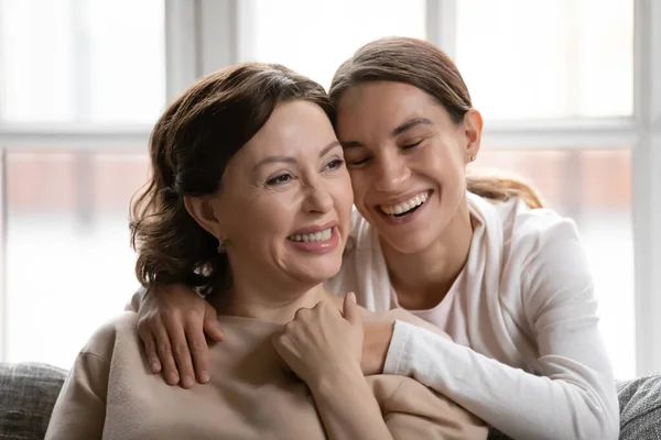 Smiling middle-aged mother and adult daughter hug at home