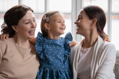 Üç nesildir gülümseyen kadınlar kanepede birlikte rahatlar.