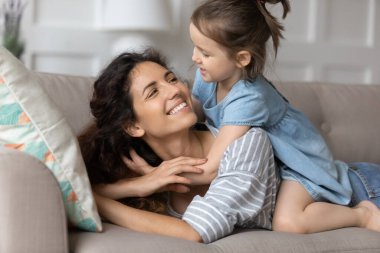 Gülümseyen anne ve küçük kız kanepede kucaklaşıyorlar.