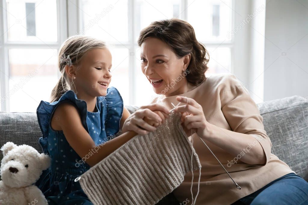 Happy mature grandmother teach small granddaughter knitting