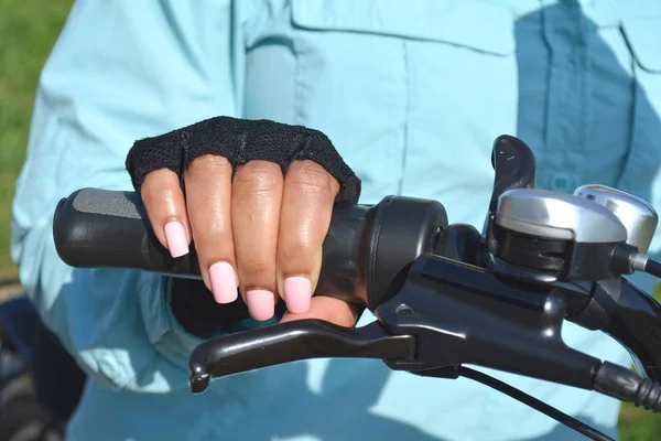 Woman hand with bright pink nails on the bicycle handle.