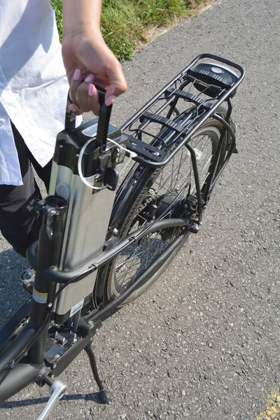 Vrouwen houden van de accu van de elektrische fiets in de buurt van haar e-fiets. — Stockfoto