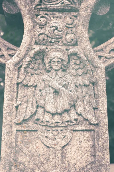 Outdoor weathered statue of angel on cross.