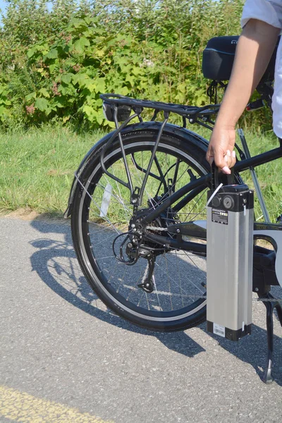 Vrouwen houden van de accu van de elektrische fiets in de buurt van haar e-fiets. — Stockfoto