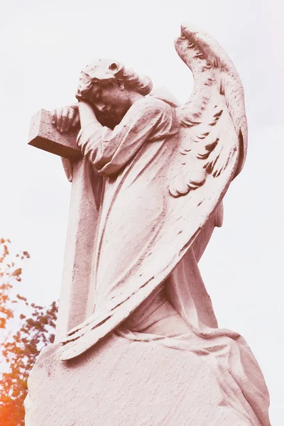 Outdoor weathered statue of angel on cross. Guardian angel.