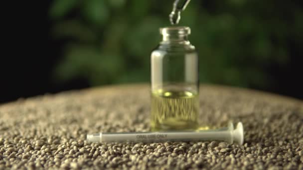 Deslizamiento y cambio de enfoque mientras el gotero de pipeta dosifica aceite de cbd. Tarro de vidrio en la alfombra de semillas de cáñamo. Concepto médico de farmacia sanitaria de nueva era. Revolución en el tratamiento del dolor y la ansiedad curativa . — Vídeo de stock