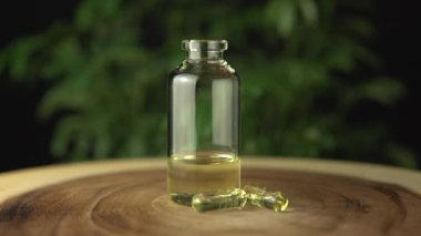Cam kavanoz şişesinde tıbbi kenevir cbd yağ yoğunlaştırılmış reçine var. Oral yönetim için taşıyıcı yağla sulandırılmış. Ahşap masa ve yeşil kenevir bitkisi arka planı.