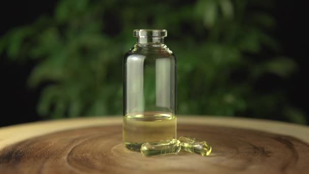 Extrémní uzavření skleněné lahvičky s lékařským konopným cbd olejem koncentrovaným na pryskyřici a zředěným nosným olejem pro perorální podání. Na dřevěný stůl a zelené konopí rostliny pozadí. — Stock video