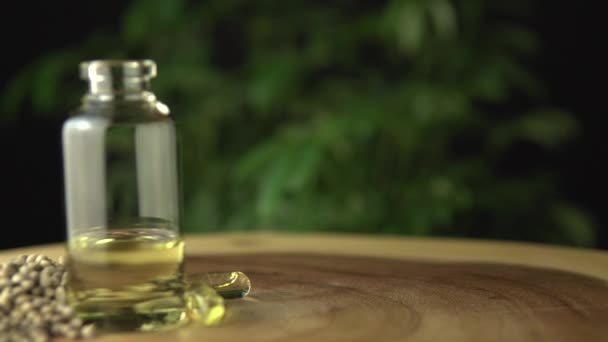 Extreme close-up van de glazen potfles met medicinale cannabis cbd olie geconcentreerde hars doseren en verdund met een drager olie voor orale toediening. Op hout tafel en groene hennep plant achtergrond. — Stockvideo