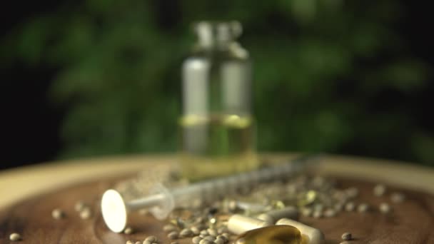 Focus shift. Medical cannabis hemp seeds various medications. Pills, THC capsules, cbd oil, syringe and glass jar bottle with concentrate on the wooden table near green marijuana plant macro closeup. — Stock Video