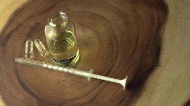 Yukarıdan bakıldığında, çember şeklinde ahşap bir ağaç halkası masası ve şırıngada oral kullanım için gerekli kenevir yağı ve küçük cam kavanoz şişesi var. Yağ kapsülleri tedavi için bir seçenektir. Kapat..