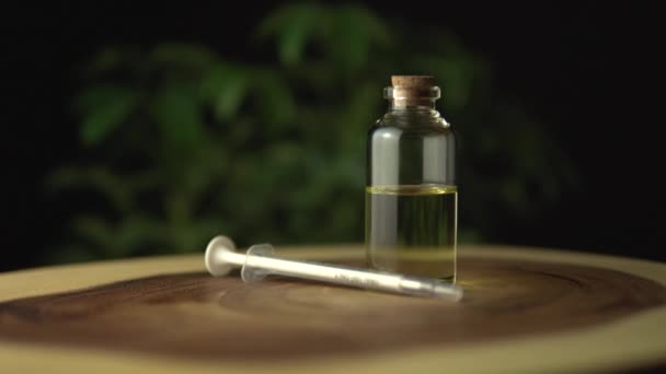 Vista muy cercana del aceite de CBD y la jeringa oral para aliviar la ansiedad y el estrés cerca del frasco de vidrio en la mesa del anillo del árbol del círculo de madera con patrón de línea de ondulación. Revolución en el tratamiento del dolor y la curación . — Vídeo de stock