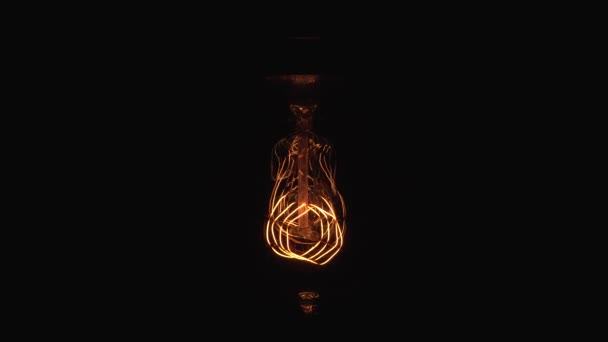Migająca żarówka wolframowa na czarnym tle. Okresowe przyciemnianie starych żarówek Edison w ciemności. Problemy z elektrycznością lub koncepcja horrorów. — Wideo stockowe