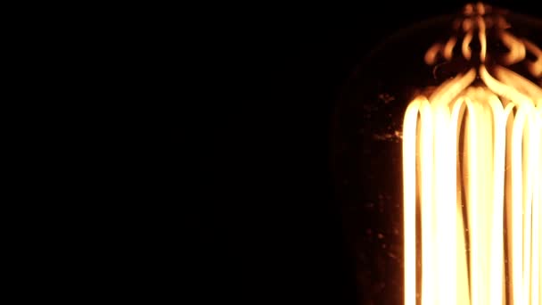 The incandescent Edison bulb lamp with a tungsten filament brighten and moving swinging while spinnig. Yellow light over black background rotation, close up view. Revealing details from bokeh, 4k. — Stock Video