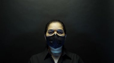 Coronavirus pathogen outbreak pandemic concept. Woman in urban protective or medical mask, looking at the camera on black background. Virus disease 2019-nCoV protection and prevention. 4k