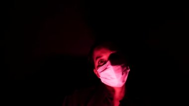 Karanlıkta ve kırmızı ışıkta cerrahi maske takan kadın. Coronavirus 'tan ya da covid 19' dan kişisel karantina izolasyonu. Küresel salgının kıyametleri ve depresyon havası.