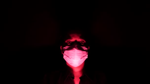 Mulher na máscara médica cirúrgica na escuridão e luz vermelha. Isolamento de quarentena em casa forçado pessoal do conceito Coronavirus ou covid 19. Apocalipses e depressão humor de epidemia global . — Vídeo de Stock