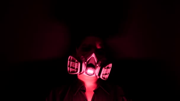 Frau in der schweren Biohazard medizinischen Maske in der Dunkelheit und Rotlicht. persönliche Zwangsquarantäne zu Hause gegen Coronavirus oder Covid-19-Konzept. Apokalypsen und depressive Stimmung. — Stockvideo