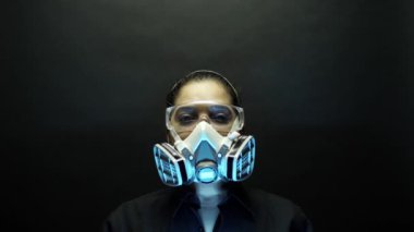 Coronavirus pathogen outbreak pandemic biohazard concept. Woman in heavy duty urban protective mask and glasses, looking at the camera on black background. Virus disease 2019-nCoV protection. 4k