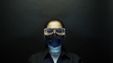 Woman in urban protective or medical mask with glasses, looking at the camera on black background. Coronavirus pathogen outbreak pandemic concept. Virus disease 2019-nCoV protection and prevention. 4k