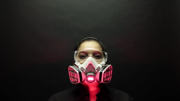 Coronavirus kórokozó járványkitörés biológiailag veszélyes fogalom. Egy nő nagyteljesítményű városi védőmaszkban és szemüvegben, fekete háttérrel a kamerába néz. Vírus betegség 2019-ncov védelem. 4k — Stock videók