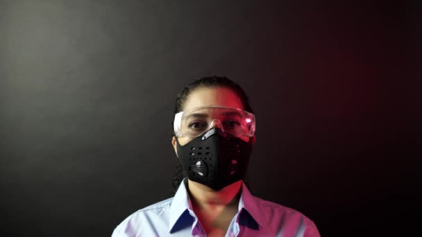Mulher em máscara protetora urbana ou médica com óculos, olhando para a câmera em fundo preto. Conceito de pandemia de surto de patógeno por coronavírus. Doença por vírus 2019-nCoV proteção e prevenção. 4k — Vídeo de Stock