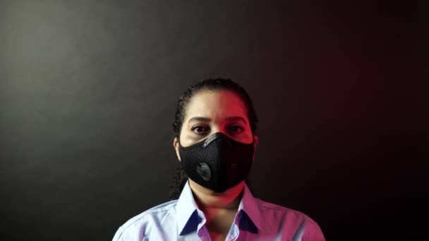 Coronavirus pathogen outbreak pandemic concept. Woman in urban protective or medical mask, looking at the camera on black background. Virus disease 2019-nCoV protection and prevention. 4k — ストック動画