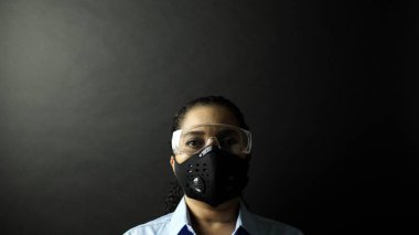 Kentsel koruyucu ya da tıbbi maskeli gözlüklü bir kadın siyah arka plandaki kameraya bakıyor. Coronavirus patojen salgını konsepti. Virüs Hastalığı 2019-Ncov Koruma ve Önleme. 