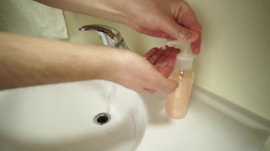Erkek ellerini beyaz havuzda yıkar ya da sıvı sabun ya da vücut köpüğüyle kabuğunu batırır. Ellerin derisini dikkatlice ve dikkatlice temizliyor. Coronavirus enfeksiyonu ve COVID 19 önleme.