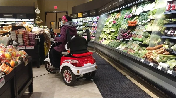 Toronto, Ontario, Kanada - 27 Mart 2020: Coronavirus salgını sırasında, tıbbi maskeli ve eldiven alışverişi yapan gezici scooterlı engelli kadın. Cep telefonu.