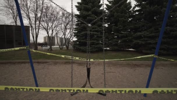 Toronto, Ontario, Canadá - 7 de abril de 2020: Swing set abandonado y bloqueado debido al cierre de alerta de coronavirus COVID-19, todos los servicios de los parques, incluidos los parques infantiles, están cerrados. Cinta de precaución amarilla envuelta . — Vídeos de Stock