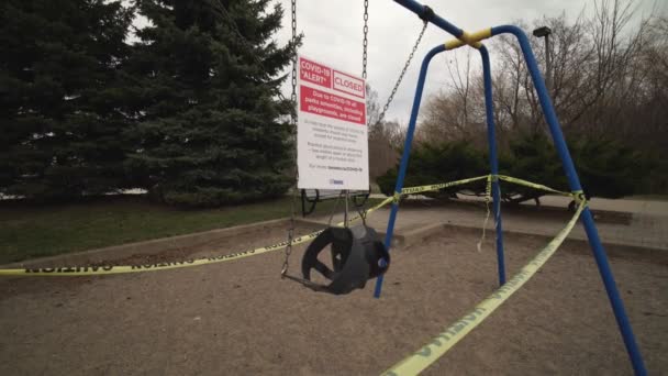 Toronto, Ontario, Kanada - 7 April 2020: Set Swing ditinggalkan dan dikunci karena penutupan peringatan penobatan COVID-19, semua fasilitas taman, termasuk taman bermain, ditutup. Pita peringatan kuning dibungkus. — Stok Video