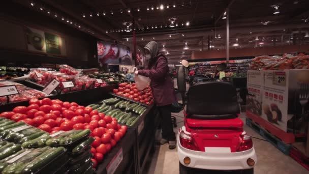 Toronto, Ontário, Canadá - 7 de abril de 2020: Mulher com deficiência na scooter de mobilidade na máscara médica e luvas de compras no supermercado durante o surto de pandemia do coronavírus COVID-19 . — Vídeo de Stock